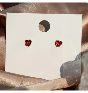 Close-up of heart-shaped red zircon stud earrings with golden prong setting on satin