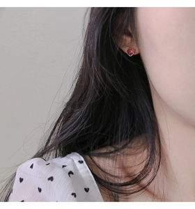 Close-up of s925 silver heart earrings with red cubic zirconia on a female model's ear