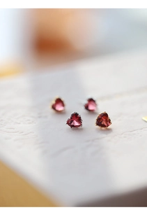 Macro shot of 5mm heart-cut red zircon stud earrings in silver and gold claw settings