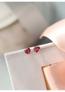 Macro shot of s925 silver heart stud earrings with red gemstones on silk background
