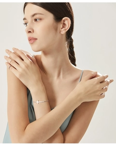 Dettaglio del bracciale con croce minimalista e anelli sovrapposti sulla modella