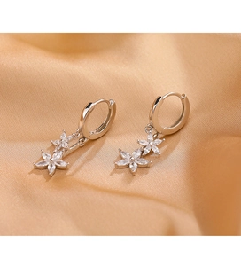 Détail de créoles en argent avec pendentifs fleurs en zircon étincelant sur du satin