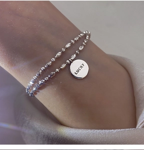 Close-up of a shimmering double-layer beaded bracelet with a Lucky engraved pendant