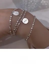 Detail of layered silver bracelets featuring a Lucky engraved charm on a woman's wrist