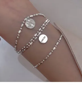 Close-up of a layered silver bead bracelet with engraved Lucky charm on female wrist