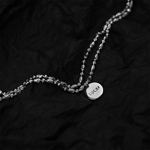 Macro shot of silver minimalist necklace featuring a lucky round tag with wavy twisted chain