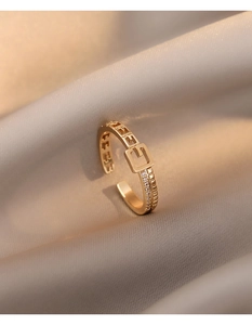 Détail d'une bague dorée ajustable avec lettres évidées et pavage de diamants latéraux