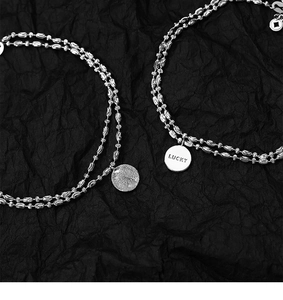 Detail of double-layer silver bracelet with Lucky engraved charm and frosted disk pendant