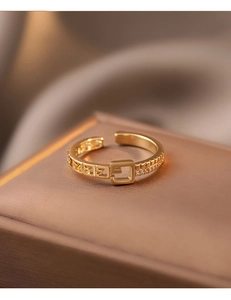 Gros plan d'une bague boucle dorée avec motif carré et pierres étincelantes incrustées