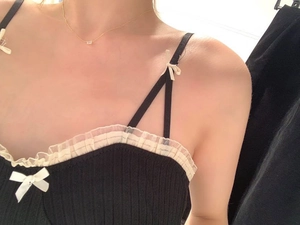 Dettaglio di canotta nera in maglia con fiocco bianco e finiture in pizzo fine