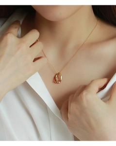 Dettaglio di una collana dorata minimalista con pendente ovale sulla clavicola di una donna