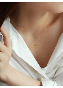 Dettaglio della collana con ciondolo ovale dorato a torsione indossata da una modella
