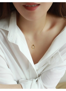 Dettaglio ravvicinato di una collana dorata con pendente ovale su una camicia bianca