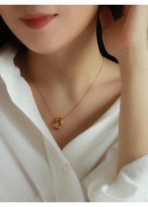 Dettaglio della collana dorata con pendente Mobius indossata da una modella in bianco