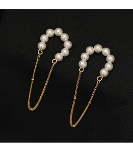 Close-up of vintage pearl tassel ear clips with golden chains on black fabric texture