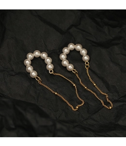 Close-up of elegant pearl ear cuffs with long gold metal chain tassels on black background