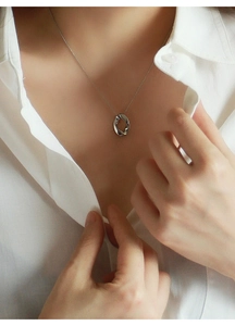 Dettaglio di una collana con pendente ovale irregolare indossata su camicia bianca