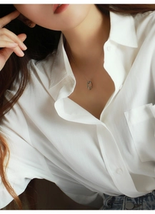 Dettaglio di una collana d'argento minimalista con ciondolo ovale cavo su camicia