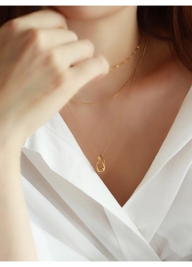 Dettaglio di collane geometriche dorate a strati con pendente ovale su camicia bianca