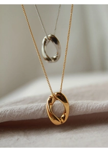 Dettaglio di collane con pendente ovale intrecciato oro e argento su tessuto beige