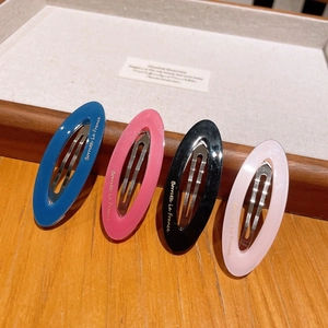 Detail of four acetate oval hair clips in blue, pink, and black on a wooden tray