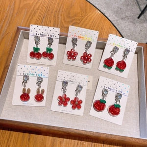 Detailed view of six pairs of red glitter resin clip-on earrings in assorted fruit shapes