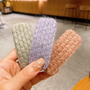 Gros plan de trois barrettes en peluche tricotée en vert pastel, violet et rose corail