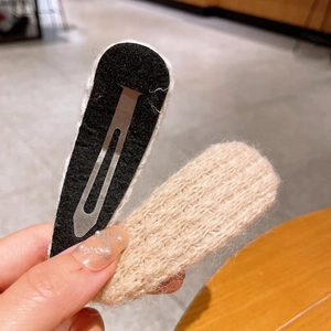 Détail d'une barrette en laine tricotée beige et base en feutre noir au style artisanal