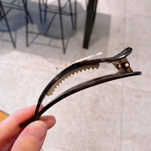 Dettaglio di una pinza per capelli nera con motivo marmorizzato grigio e molla metallica
