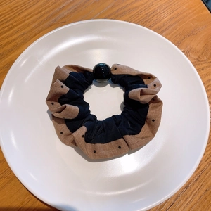 Detailed close-up of polka dot pleated scrunchie with a glossy black bead on a ceramic dish