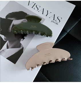 Detail of Morandi-colored acetate hair claws in dark green and apricot with gold lettering