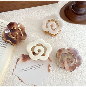 Detail of elegant acetate flower hair claws in pearl white and marble pink on vintage desk