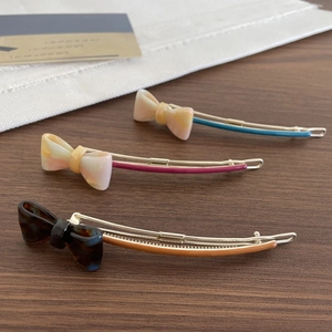 Three elegant acetate bow hair clips in various marble patterns on a wooden surface