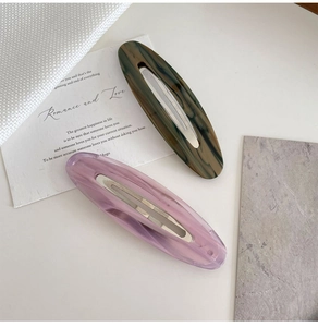 Détail de barrettes en acétate marbré avec design ovale évidé et base en métal
