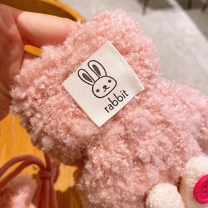 Detail eines rosa Plüsch-Kinderschals mit Hasenetikett und weißem Bommel-Akzent