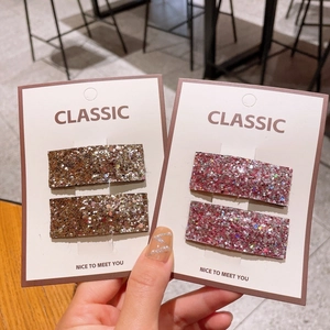 Detail of glittery rectangular hair clips in gold and rose pink on display card
