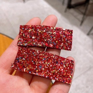 Detailed macro view of two red glitter square BB hair clips with colorful sequins