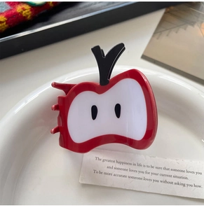 Détail d'une pince à cheveux brillante en forme de pomme rouge sur une assiette décorative