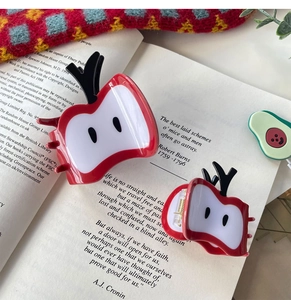 Détail de deux pinces à cheveux en forme de pomme rouge de tailles différentes sur un livre