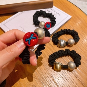Detail of black scrunchies with metallic beads and red bow charms on a wooden table