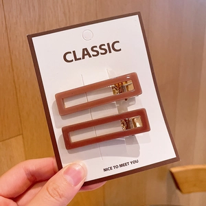 Detail of two brown acrylic rectangular hair clips with gold metal base on a white card