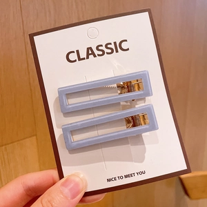 Close-up of minimalist rectangular grey-blue hair clips set on a card with gold metal base