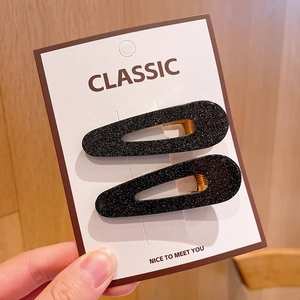 Close-up of sparkling black water-drop hair clips on card against a wooden background