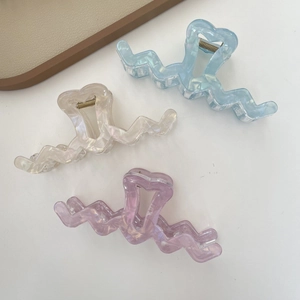 Macro detail of oversized iridescent wavy hair claw clips with heart cutout accents