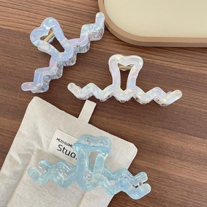 Detailed view of iridescent heart-shaped hair claws in blue and white on wooden background