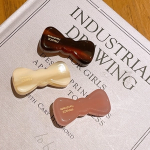 Detail view of acetate bow hair clips in tortoise shell, cream, and pink with gold lettering