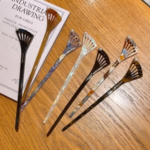 Close-up of six acetate fan-shaped hairpins with pearls displayed on a vintage book