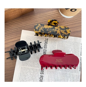 Three large acetate hair claws in tortoiseshell, black and dark red on a vintage desk