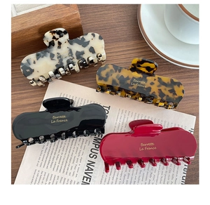 Close-up of elegant acetate hair claws in four colors with gold engraved logo text