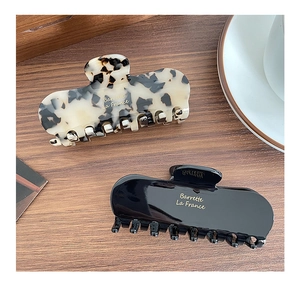 Detail of tortoise and black acetate hair claws with gold text on a wooden surface